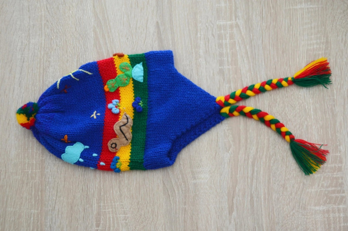 Handmade blue alpaca kids chullo hat with colorful stripes, ear flaps, and braided tassels.
