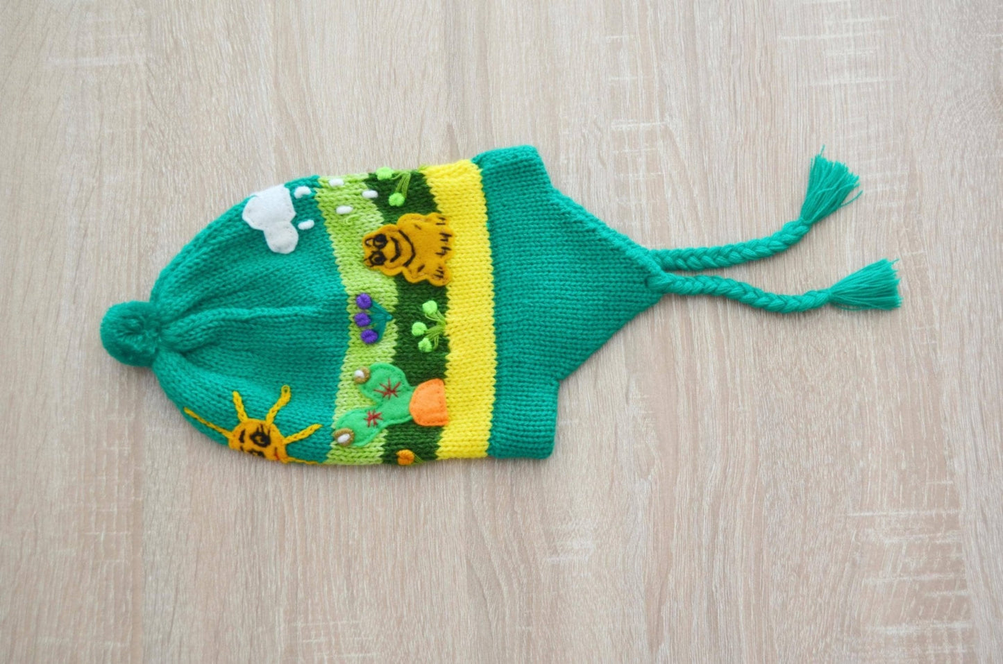 Green handmade alpaca kids chullo hat with ear flaps and colorful nature motifs.