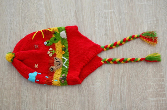 Handmade red alpaca chullo for kids with colorful animal and nature patterns, braided earflaps.