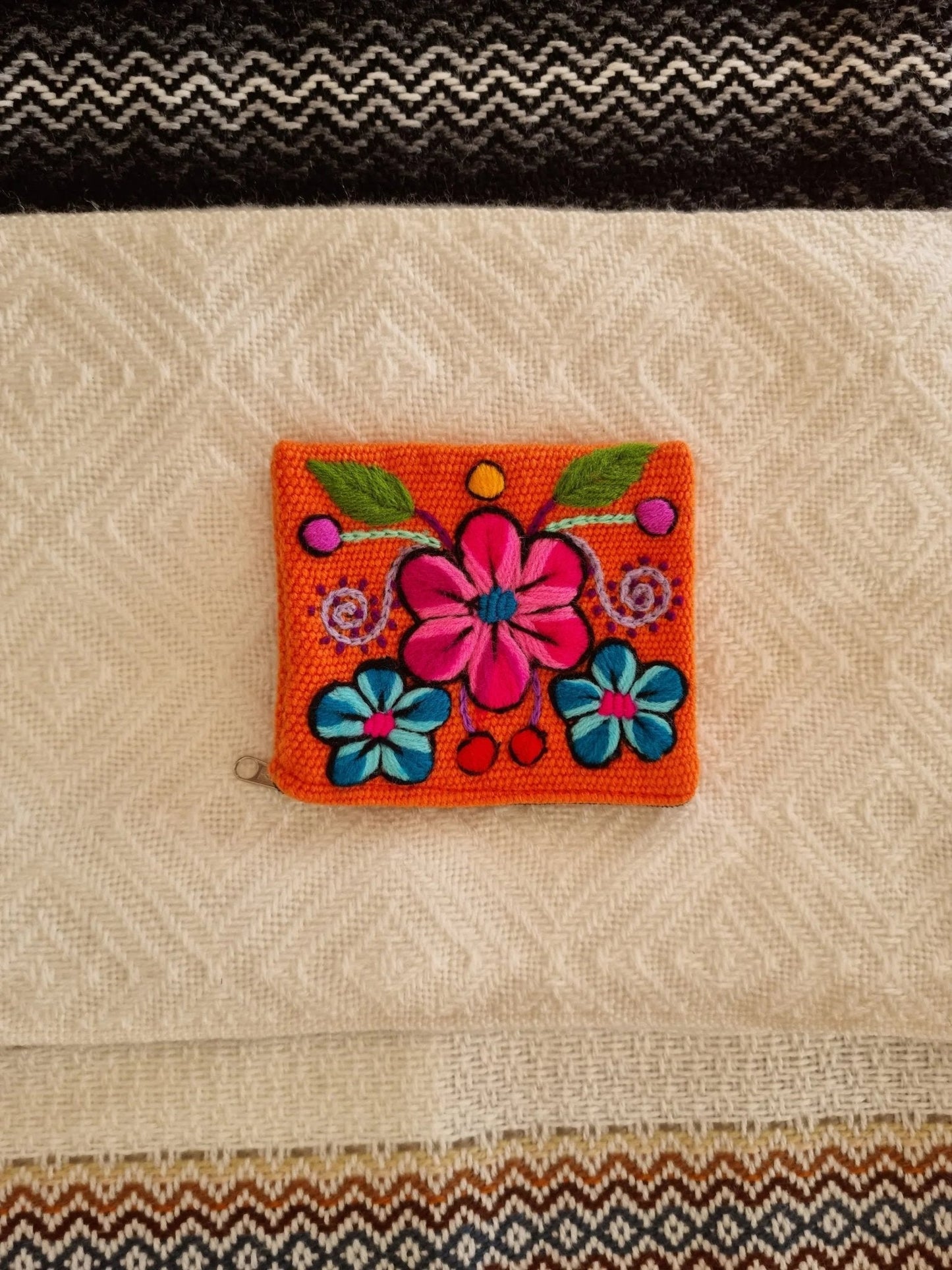 Handmade orange alpaca wool wallet with vibrant pink and blue floral embroidery.