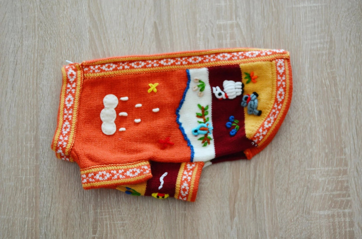 Handmade orange alpaca dog sweater with white buttons and colorful embroidered patterns.