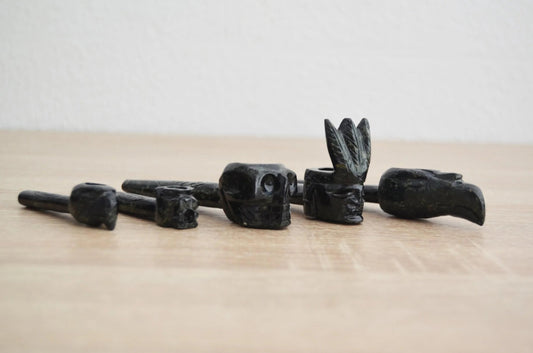 Handmade black alpaca stone smoking pipes carved with skull, animal, and tribal designs arranged on wood surface.