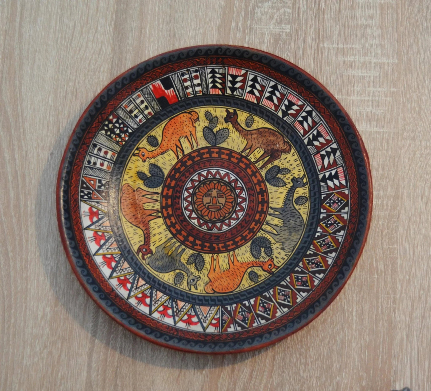 Handmade Peruvian terracotta ceramic plate with colorful alpaca and geometric patterns.