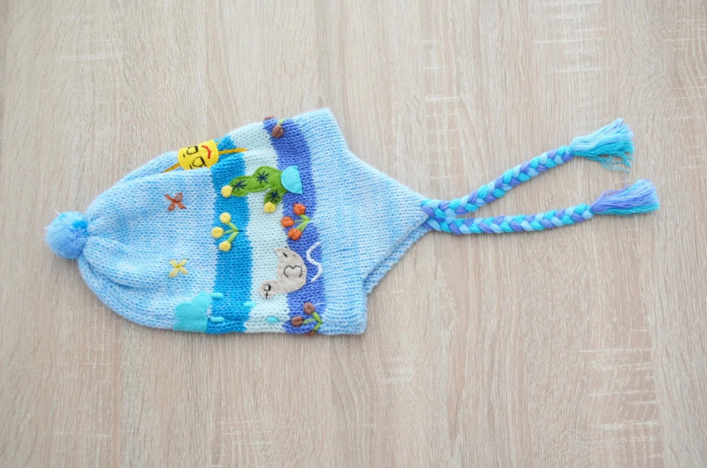Handmade alpaca kids chullo hat in light blue with colorful woven patterns and braided earflaps.