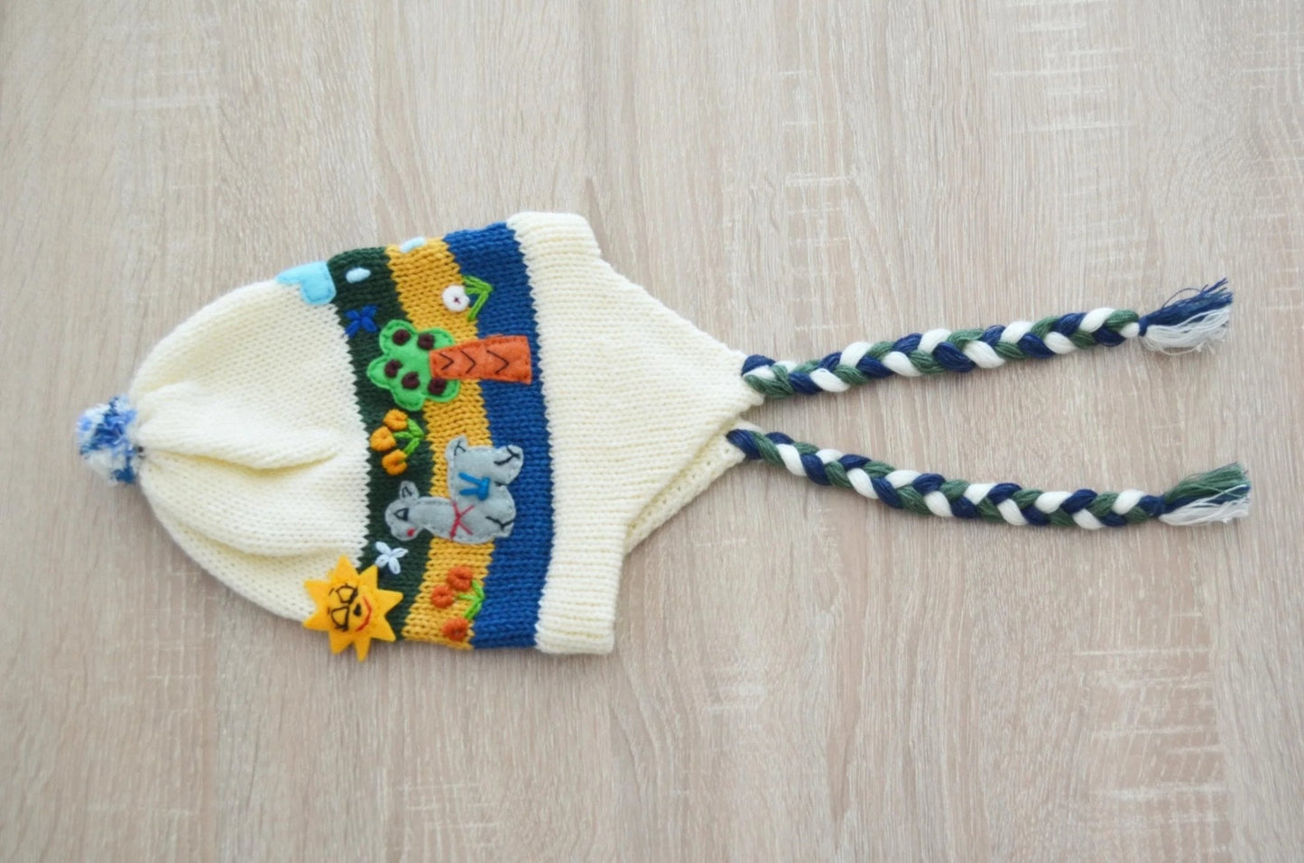 Handmade white alpaca kids chullo hat with colorful embroidery and braided earflaps.