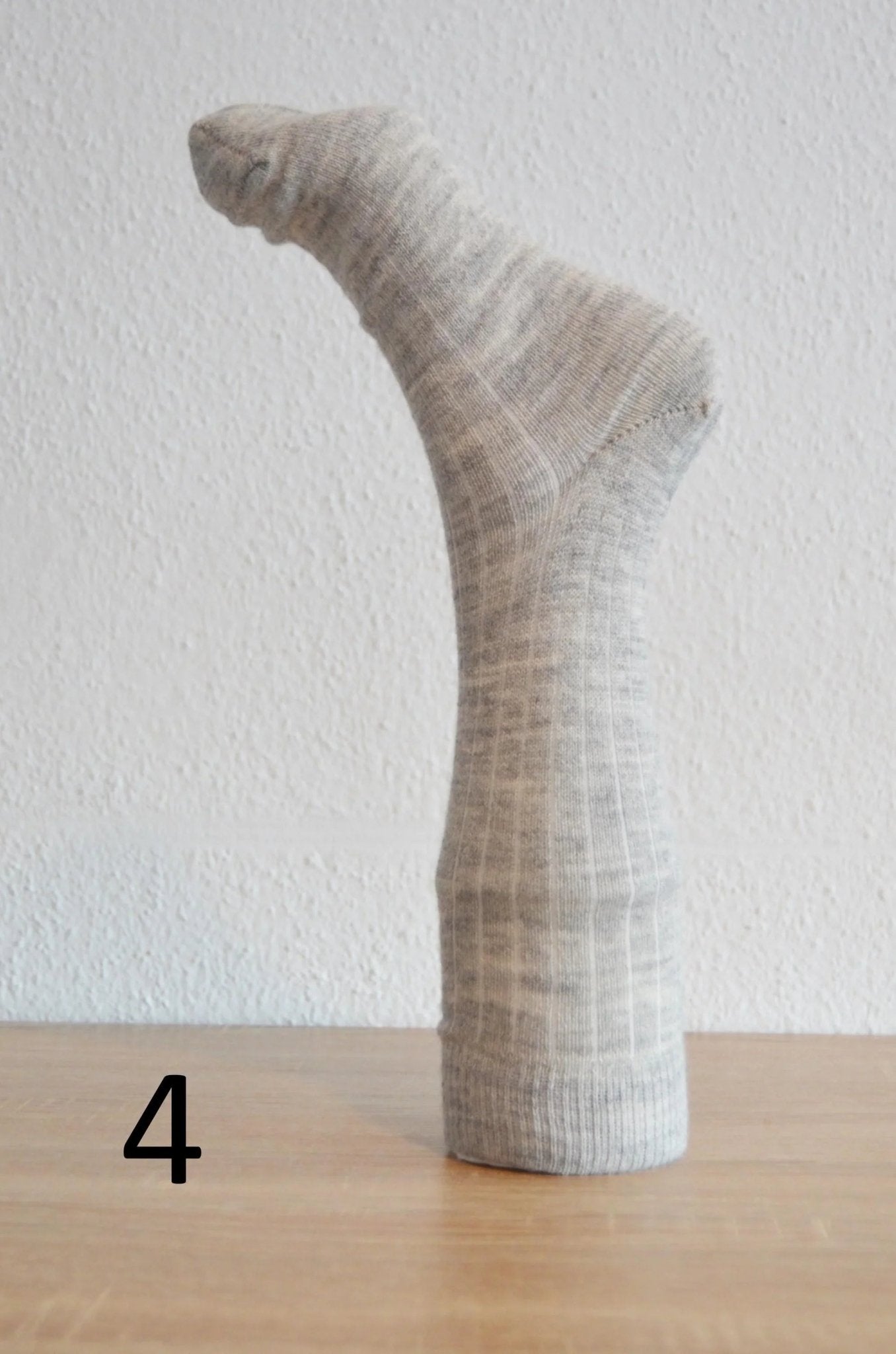 Handmade light gray alpaca and cotton sock displayed upright on wooden surface.