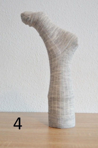 Handmade light gray alpaca and cotton sock displayed upright on wooden surface.