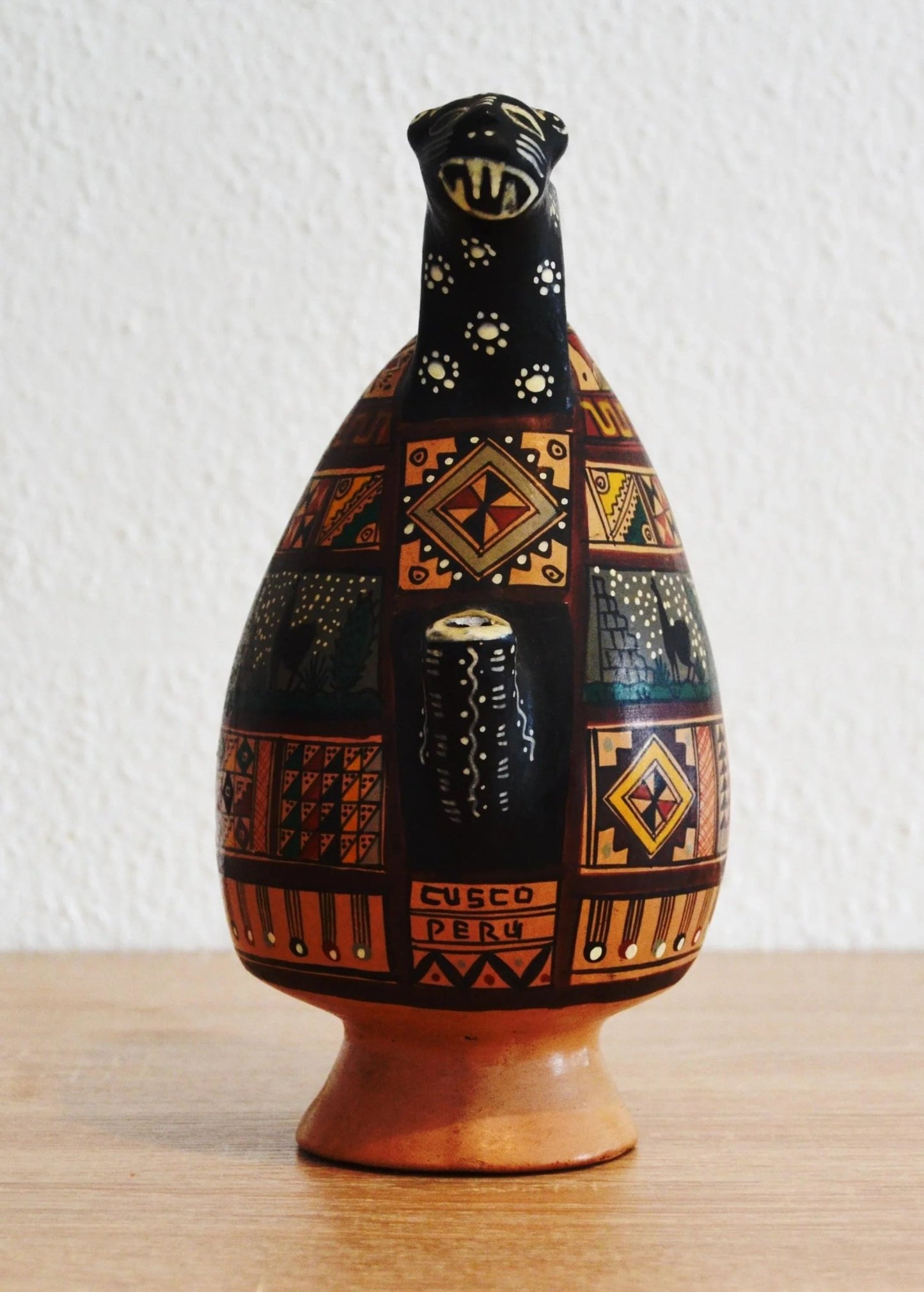 Handmade terracotta jug with colorful geometric patterns and alpaca motifs on rustic base.