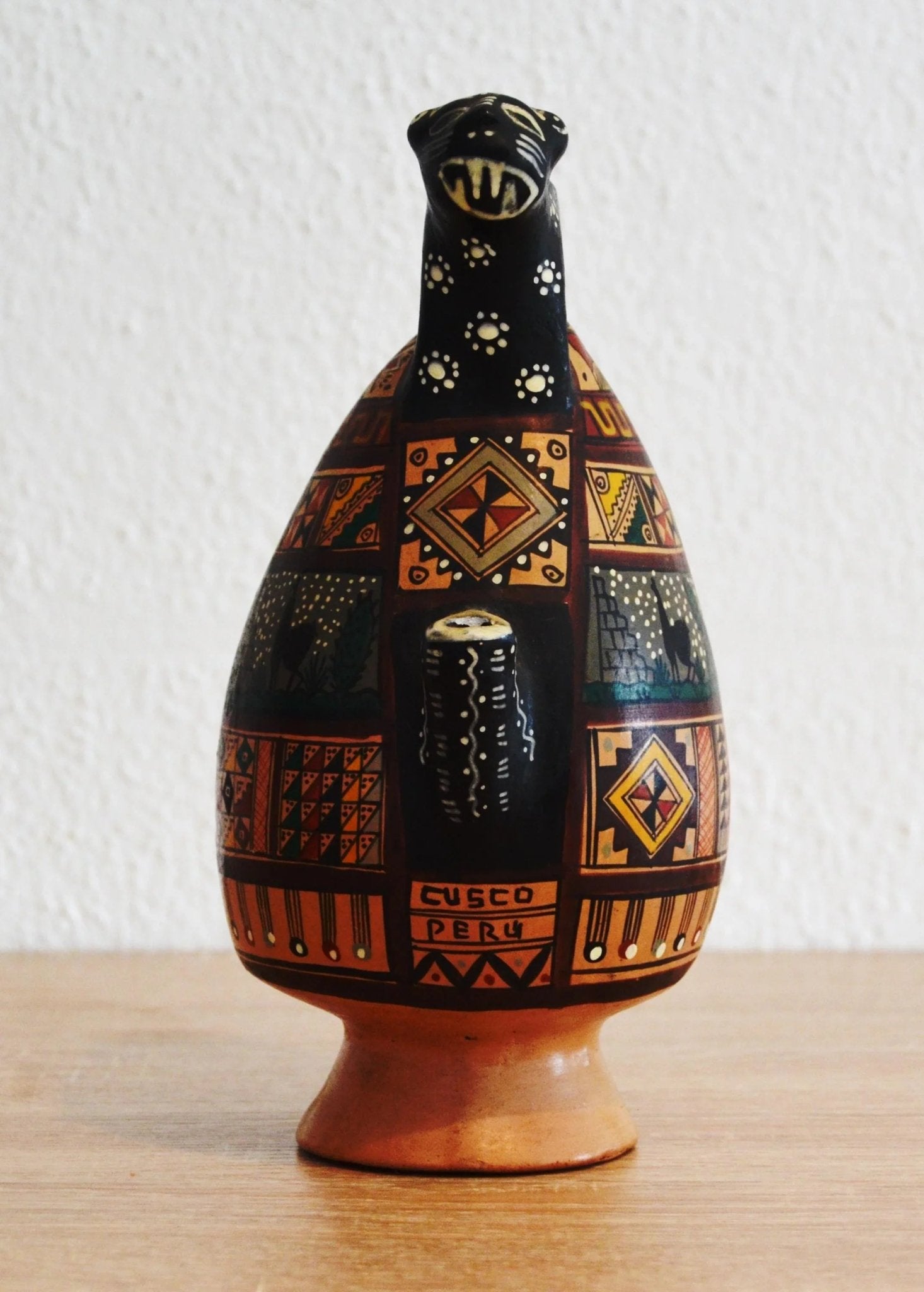 Handmade terracotta jug with colorful geometric patterns and alpaca motifs on rustic base.