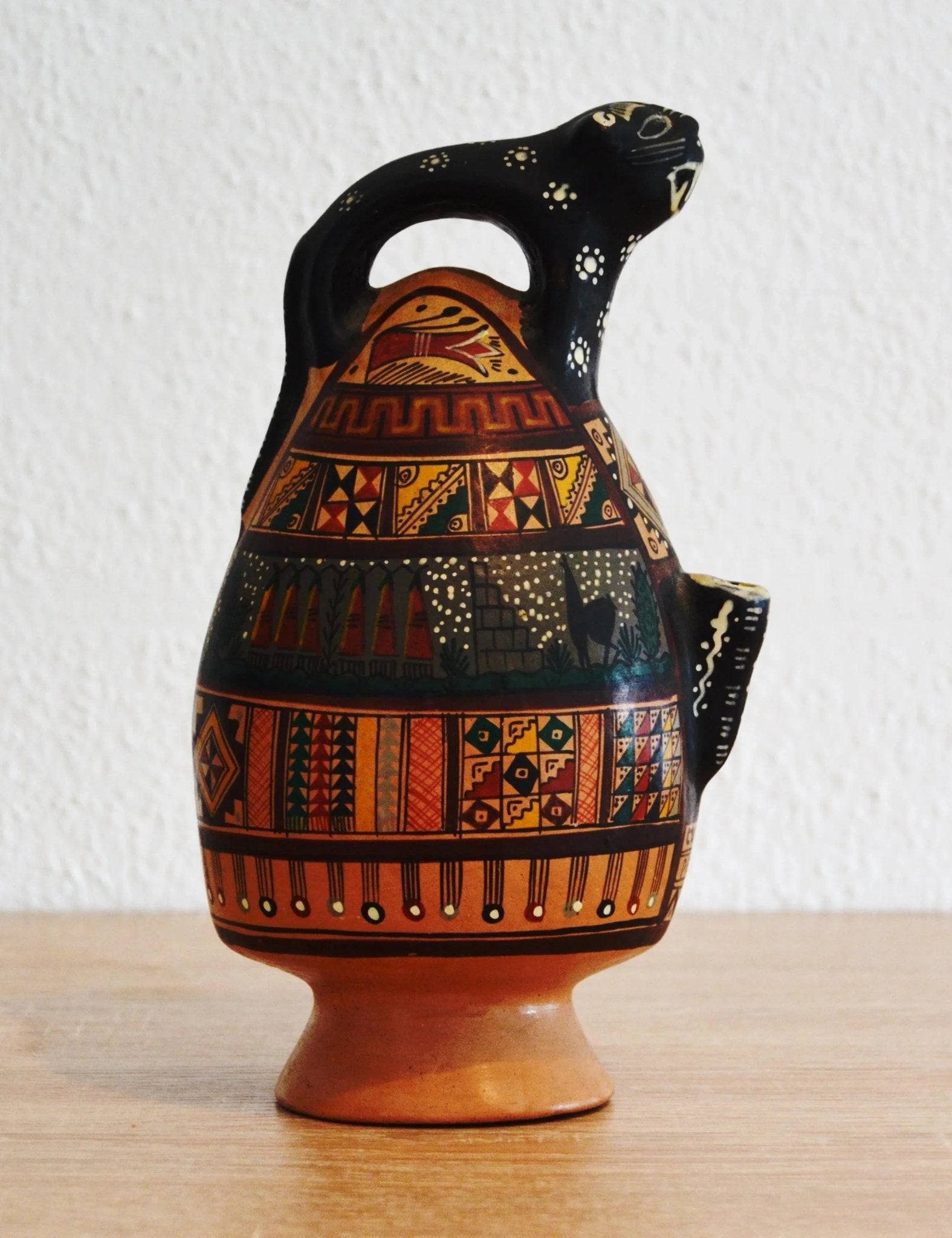 Handmade terracotta ceramic jug shaped like an alpaca with colorful geometric patterns and earthy tones.
