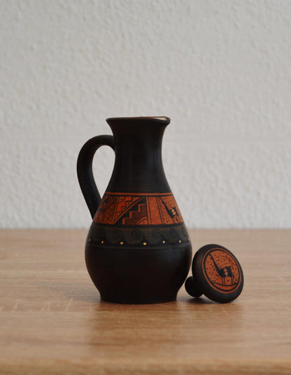 Handmade black terracotta jug with rustic orange band featuring alpaca motifs and decorative lid.