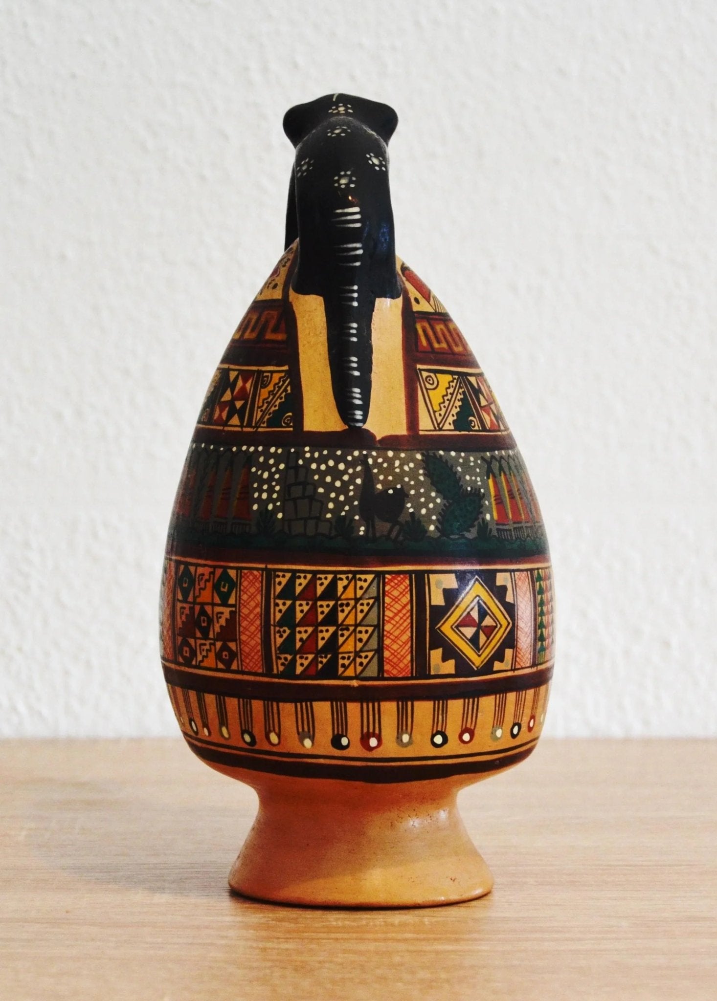 Handmade Peruvian terracotta jug with colorful geometric patterns and black alpaca figure on top.